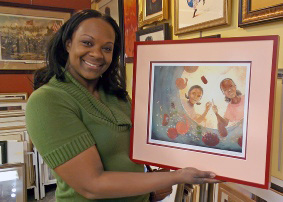 Smiling lady standing in our gallery holding up her newly framed artwork